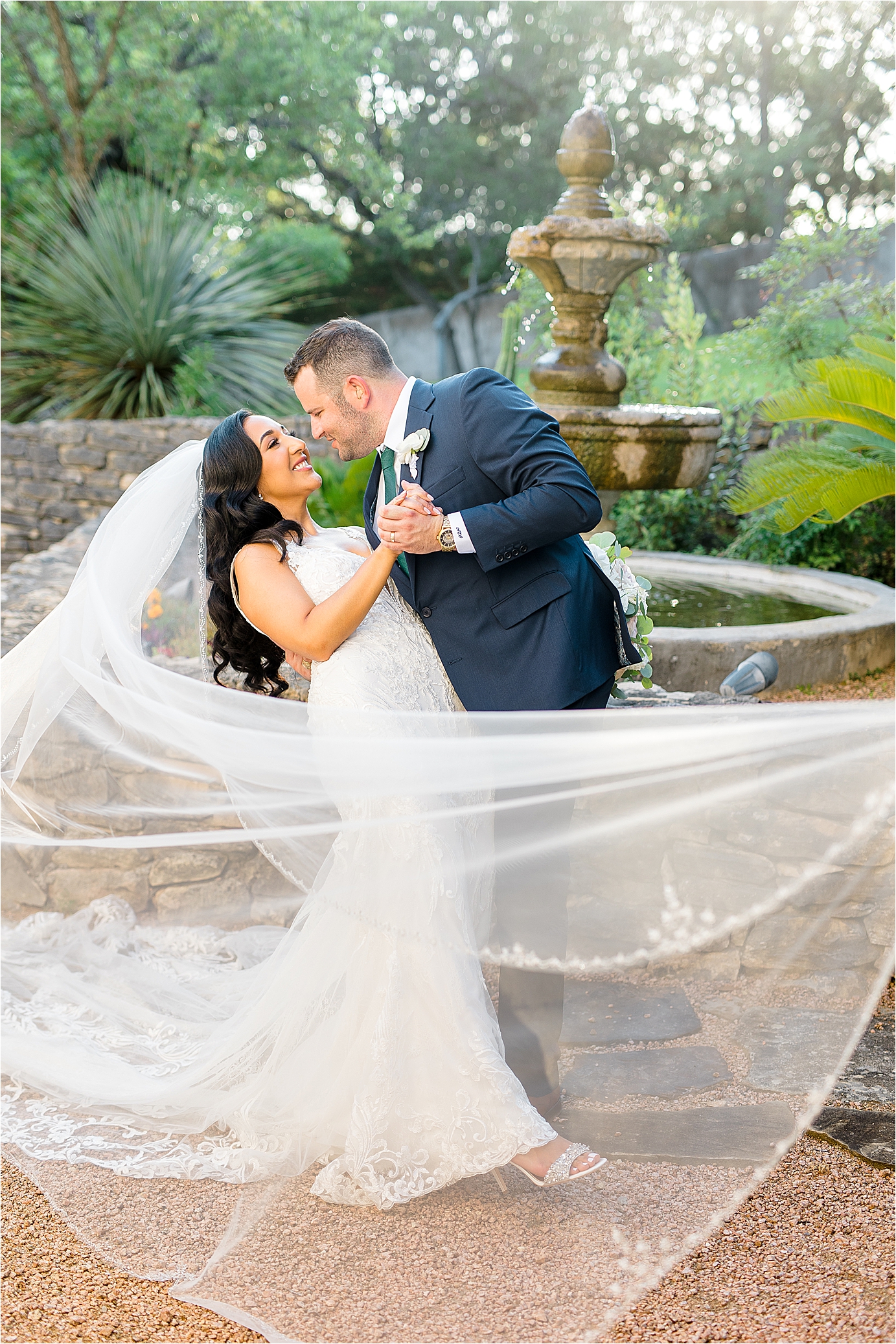 A couple dips with a veil swooped in front of them in front of a fountain at Lost Mission with Hill Country Wedding Photographer Jillian Hogan 