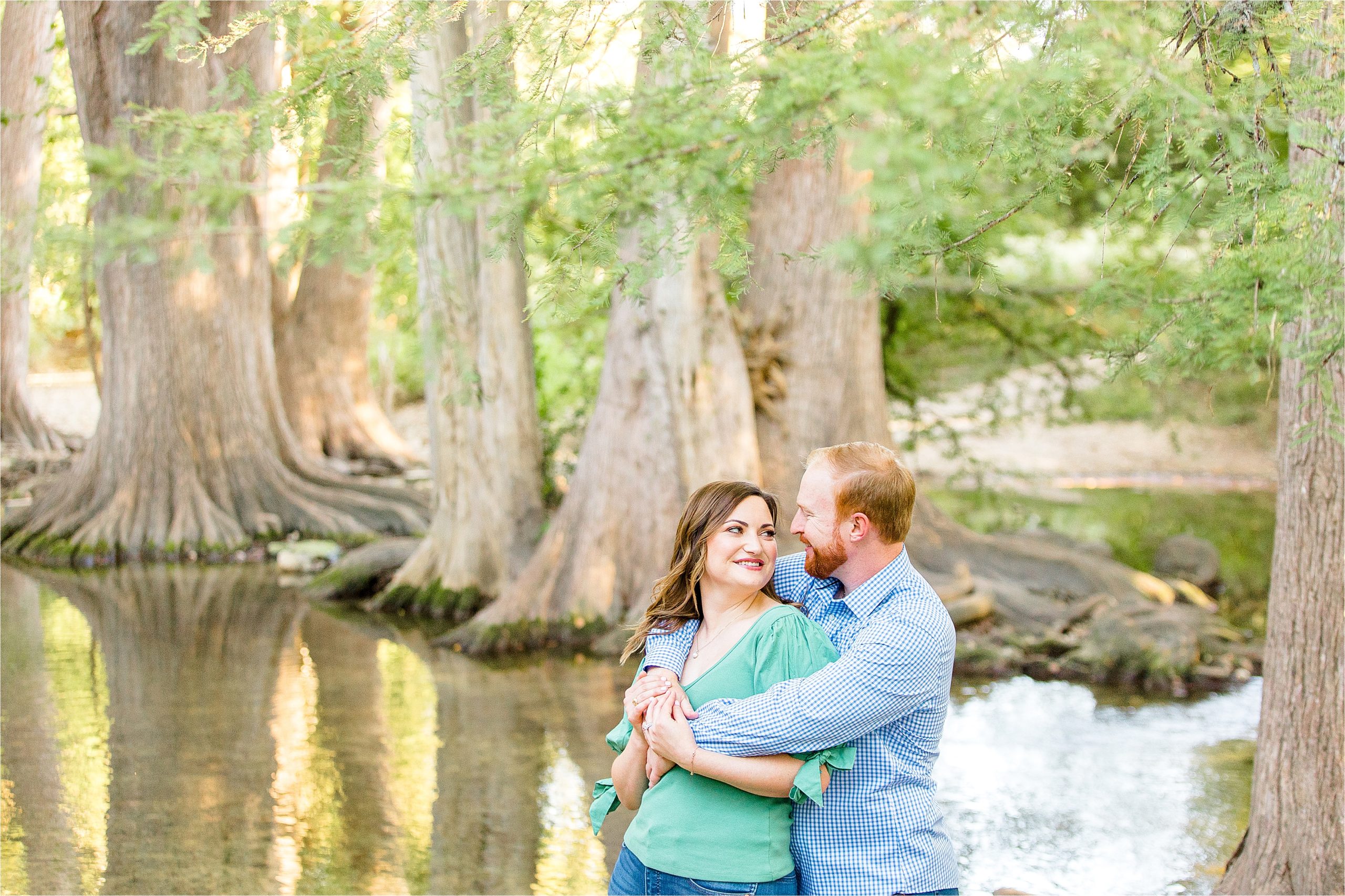 A couple embraces in front of Cibolo Creek at Cibolo Nature Center during their Fall Engagement Session in Boerne, TX with Hill Country Wedding Photographer Jilian Hogan