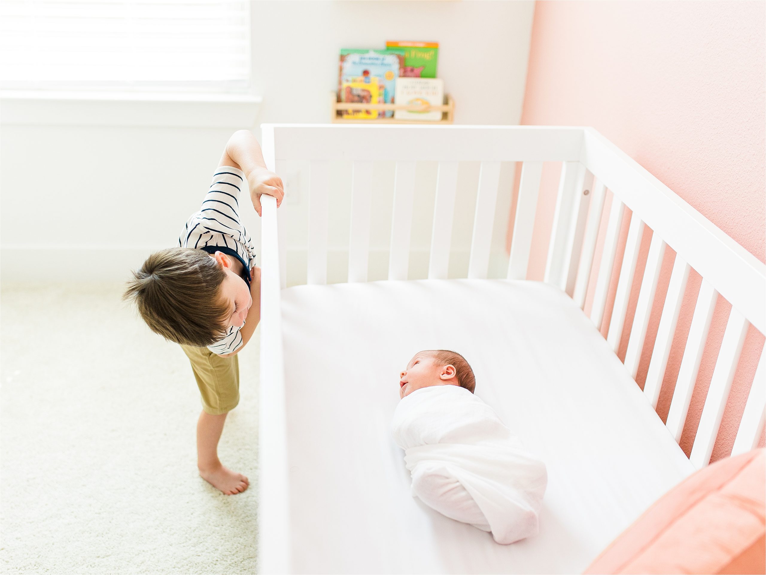 A boy peeks into his newborn sister's crib while she stares at him during photos with San Antonio Lifestyle Newborn Photographer Jillian Hogan