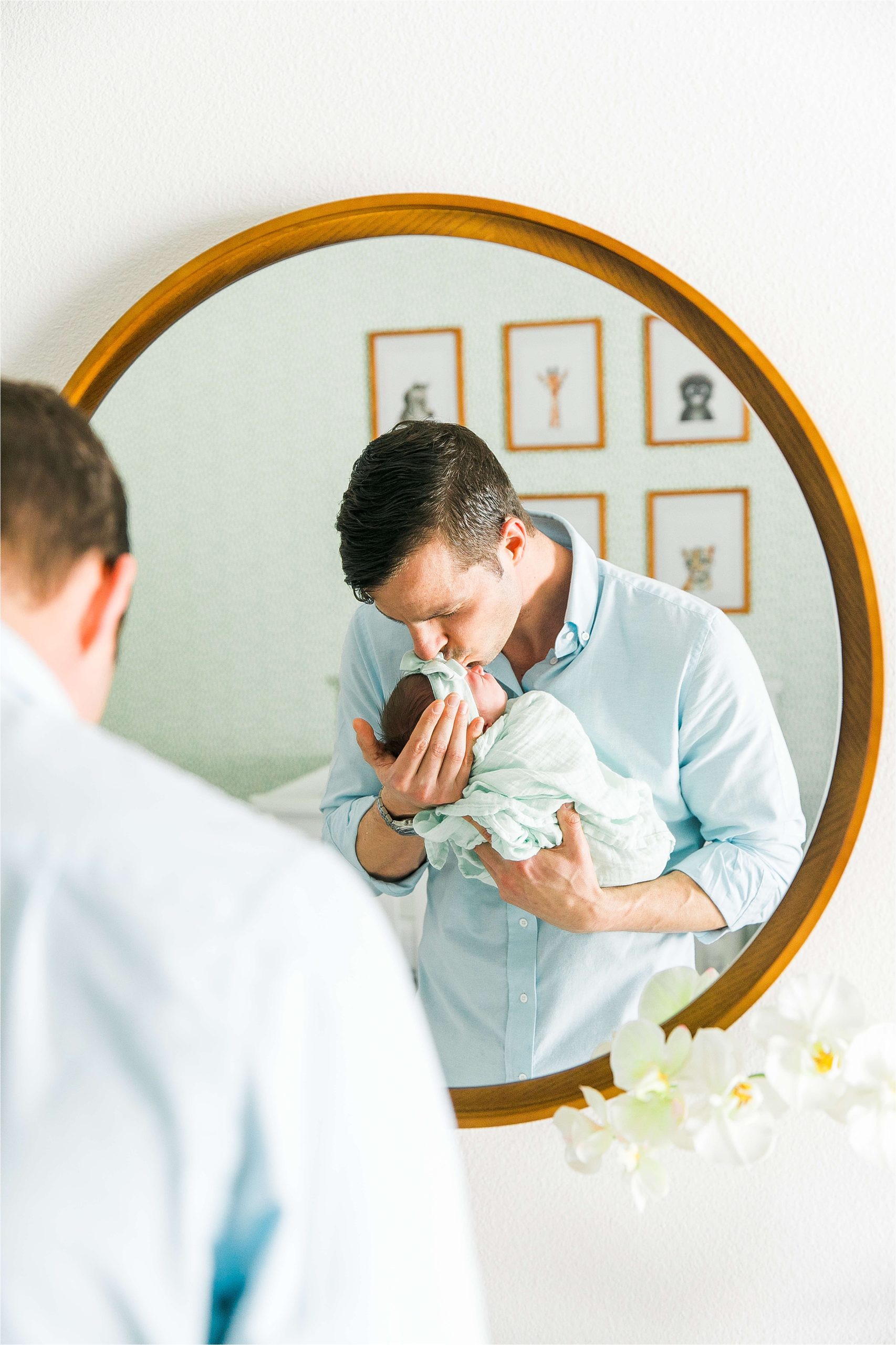 A new father kisses his newborn daughter in the mirror in her mint green nursery during their san antonio in home lifestyle newborn session 