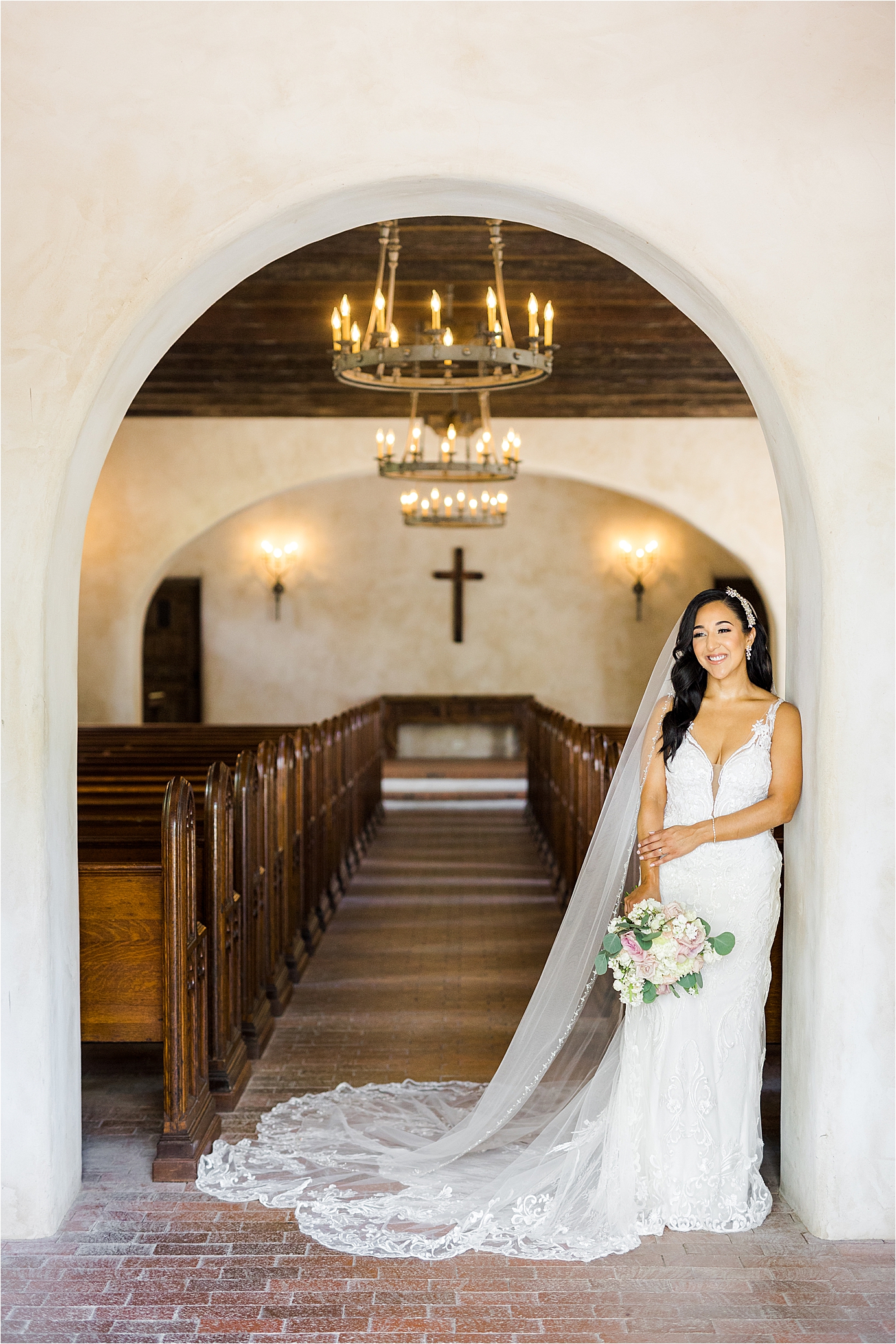 A bride poses in front of a chapel with her veil over her shoulders with pews and a cross behind her at Lost Mission with San Antonio Wedding Photographer Jillian Hogan 